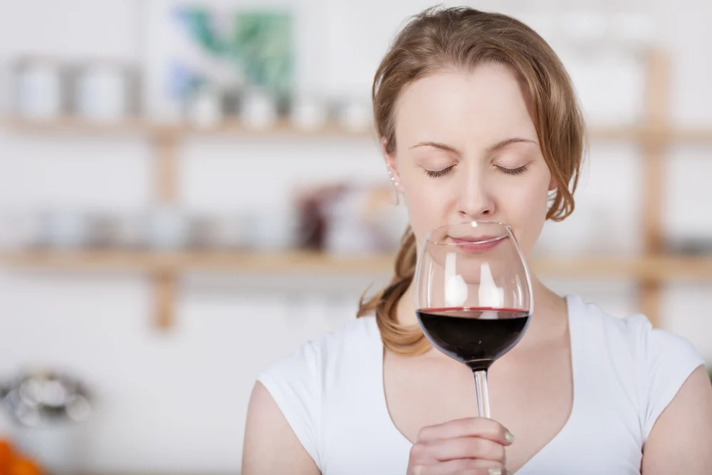 Young woman savoring the bouquet of a glass of wine as she sniffs at the glass with her eyes closed in bliss as she concentrates on the smell with copyspace indoors in the kitchen
